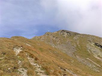 Ulteriori svolte attrezzate conducono alla successiva insellatura, dove l'evidente croce del Monte Vancomun/Hochspitz risplende alla luce del sole.