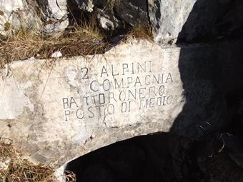 A poca distanza in una piccola conca si notano fra la vegetazione i ruderi di alcune costruzioni, in mezzo alle quali si apre l'ingresso blindato di una caverna, angusta sede di un posto di medicazione degli alpini del Battaglione Dronero.<br />