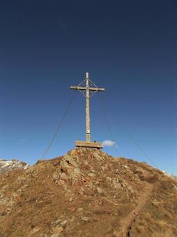 La cima dello Schönbichl/Belcolle presenta una grande croce con l'annesso contenitore del libro firme ed una rustica panca in legno.