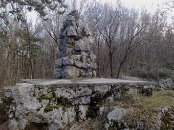 Il percorso circolare/Krožna pot, inoltrandosi nella fitta boscaglia, conduce al pannello descrittivo delle posizioni austroungariche sul rovescio del Veliki Hrib ed al caratteristico monumento austroungarico, recentemente recuperato.