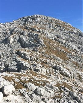 Una breve discesa conduce alla base del versante meridionale della quota minore, dove si risale senza via obbligata lungo il pendio erboso misto a roccette.