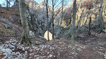 Proseguendo ancora, seguendo le indicazioni per il Sinji Vrh, in breve si raggiunge una depressione attrezzata in discesa con gradini in legno, seguendo il sentiero si può osservare da vicino la larga finestra naturale nella roccia (l'Okno), molto più amp
