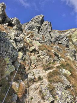 L'ÖAV, 15 rasentando sulla destra con un tratto dotato di cavo passamano una quota intermedia, risale con ulteriori attrezzature verso un caratteristico testone roccioso.